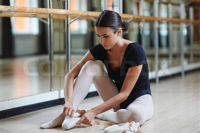 Young ballerina with pointes sitting on the floor, stock photo