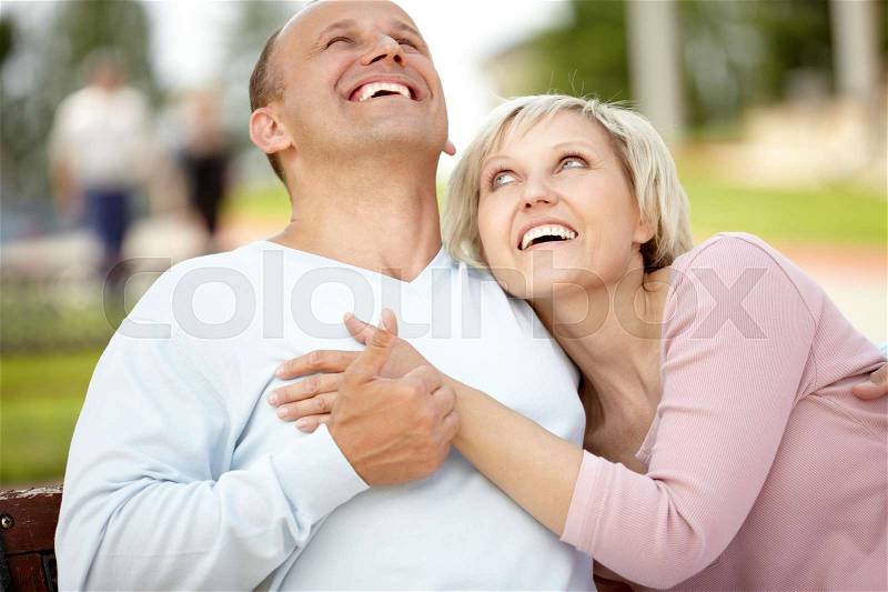 Mature couple embracing on bench and laughing, stock photo