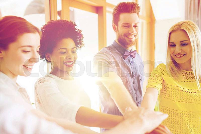 Business, startup, gesture, people and teamwork concept - happy creative team with hands on top of each other in office, stock photo