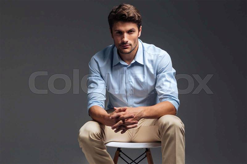 Relaxed casual handsome man in blue shirt sitting on the chair over grey background, stock photo