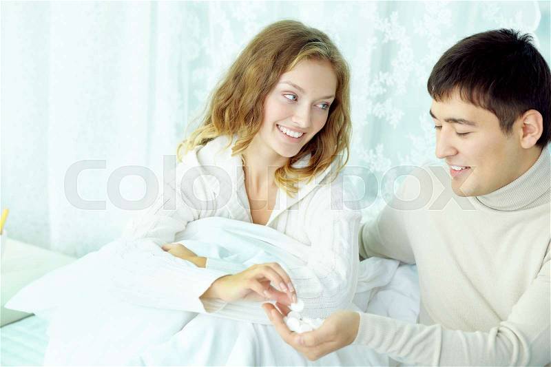 Husband offering vitamin pills to his ill wife, stock photo