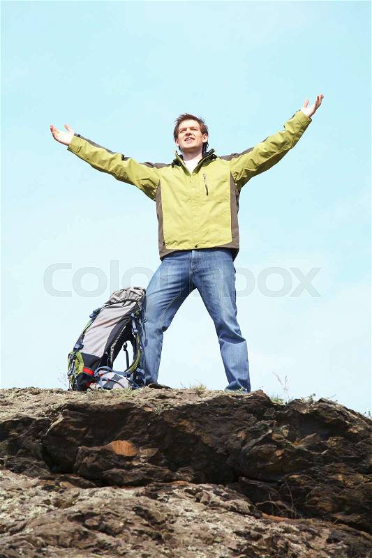 A young man with a rucksack standing at the top of some mountain stretching out his hands, stock photo