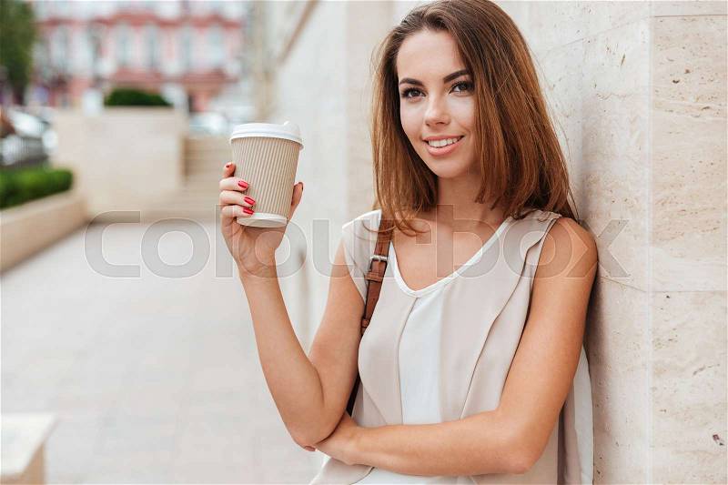 Happy woman holding take away coffee and looking at camera while standing on the street, stock photo
