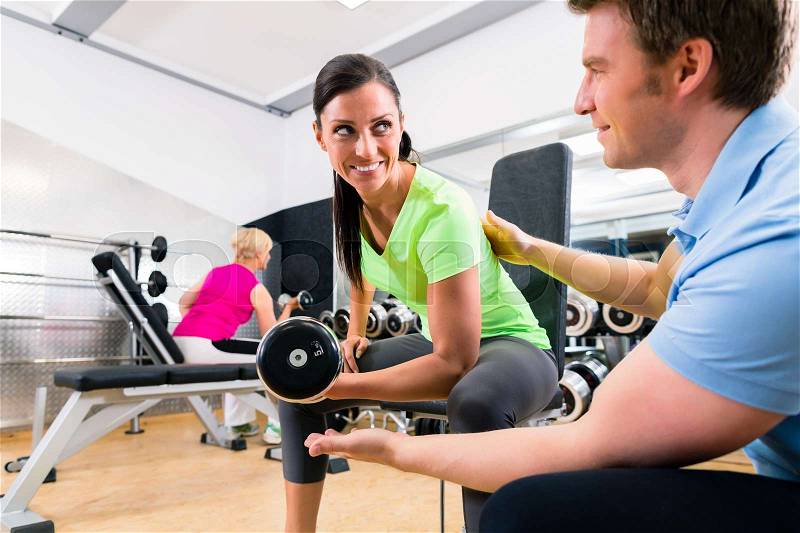 Young woman and trainer at exercise in gym with dumbbell weights, stock photo