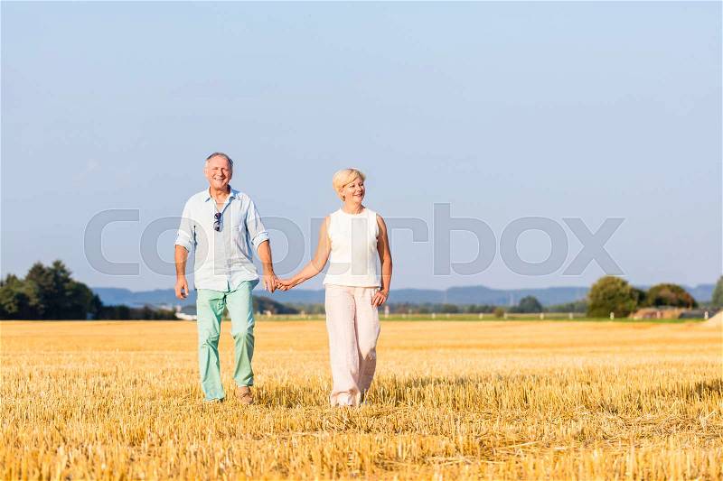 Senior woman and man holding hands having walk on field, stock photo