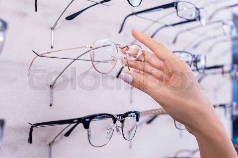 Woman taking glasses out of shelf in optician store, close up on hand, stock photo