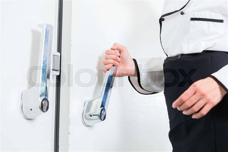 Chef opening door of cold storage in commercial kitchen, stock photo
