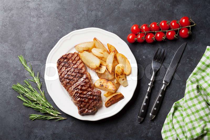 Grilled striploin steak with roasted potato on plate over stone table. Top view, stock photo