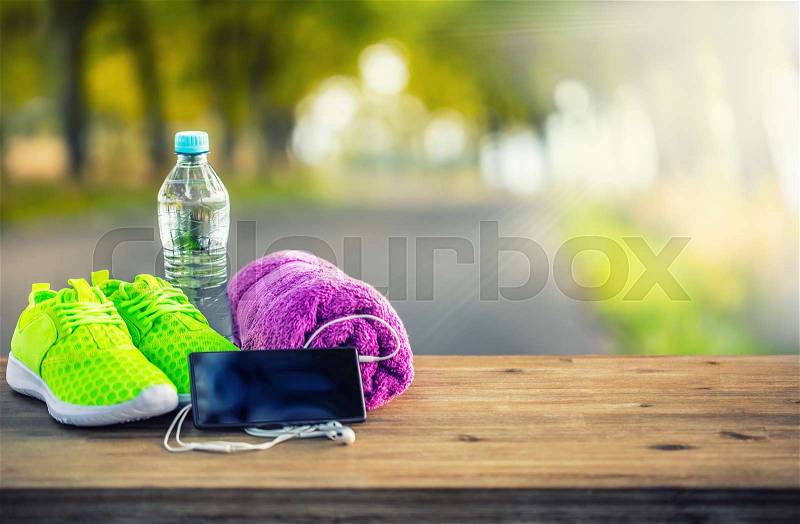 Pair of yellow green sport shoes towel water smart pone and headphones on wooden board. In the background forest or park trail.Accessories for running sport, stock photo