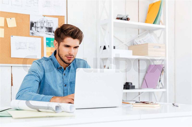 Close up portrait of a pensive young casual businessman using laptop at the office, stock photo
