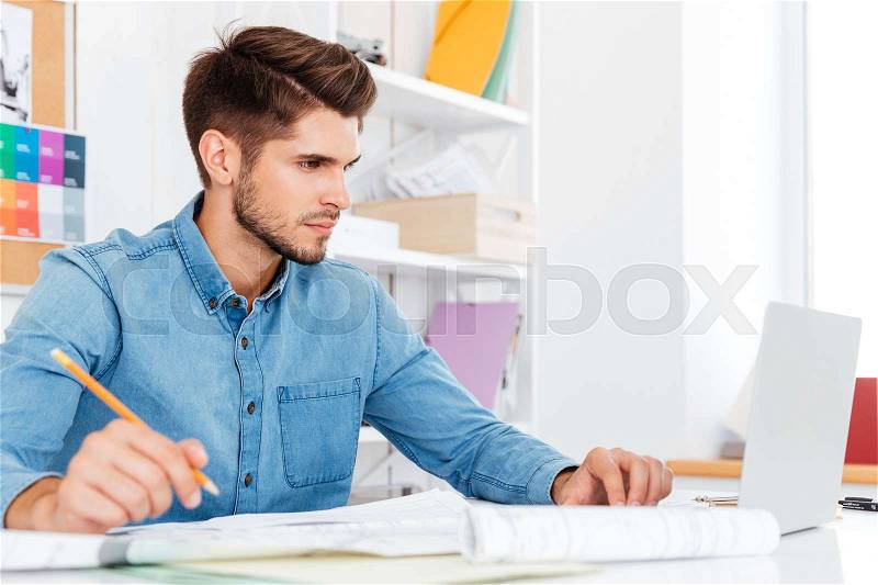 Casual young businessman looking at laptop and working with documents at the office, stock photo