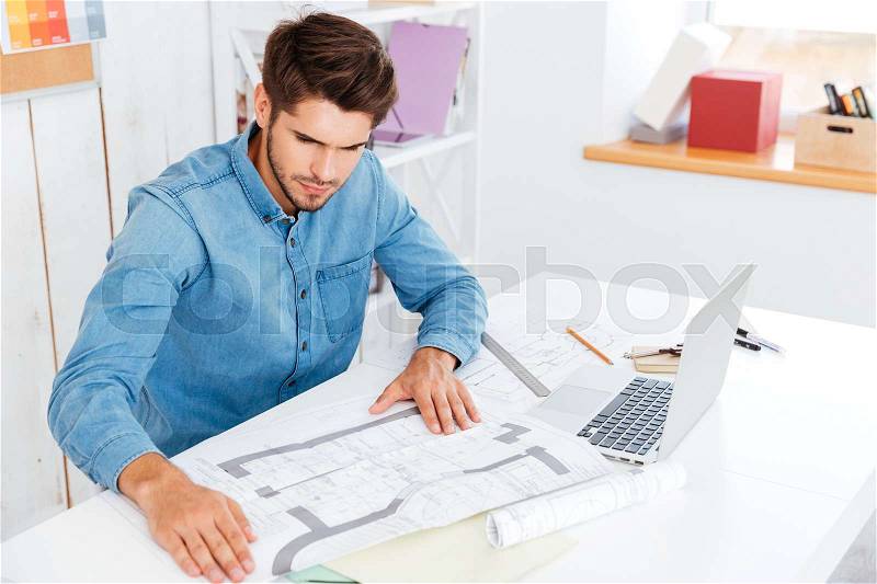 Pensive young businessman looking at diagram while sitting at the office desk, stock photo