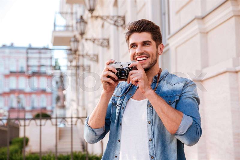Happy young man taking pictures with vintage photo camera on the street, stock photo