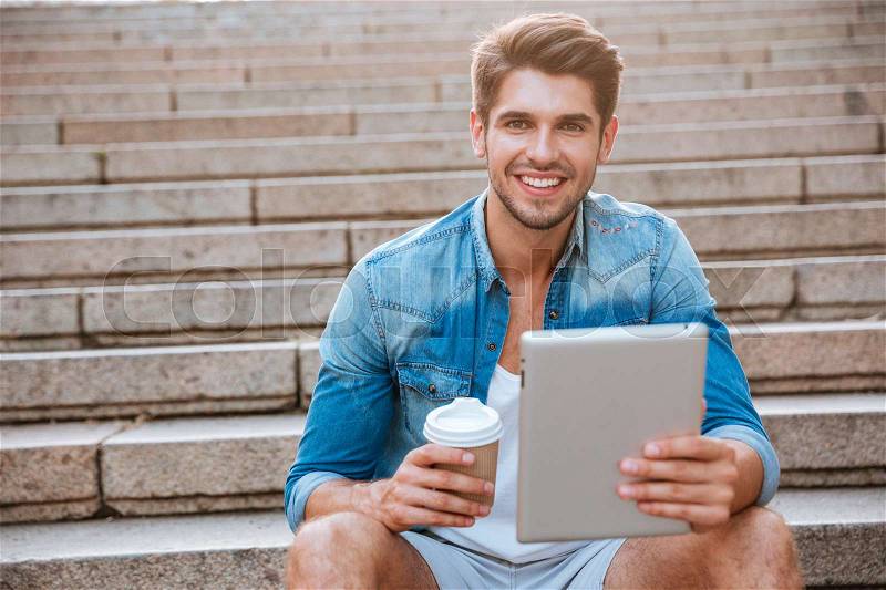Happy cheerful student with tablet and coffee cup sitting on the staircase outdoors, stock photo