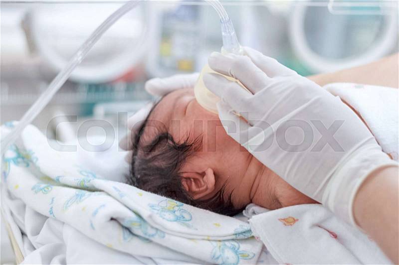 Newborn baby holding oxygen mask in nursery, stock photo