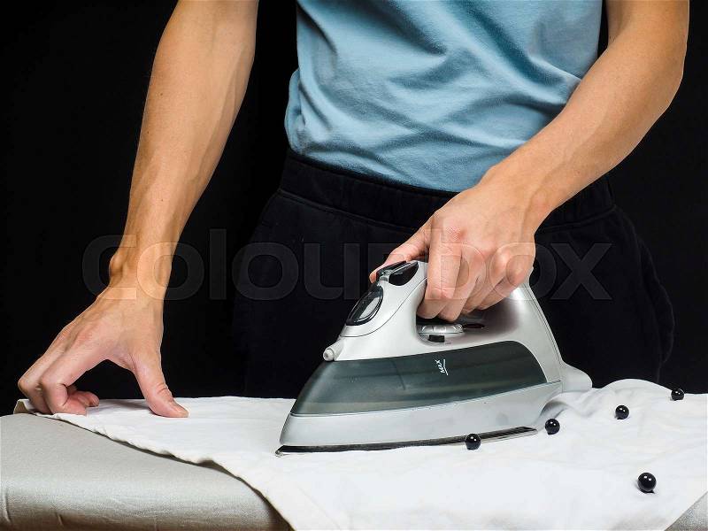 Male person using a steaming hot iron, on a white shirt, stock photo