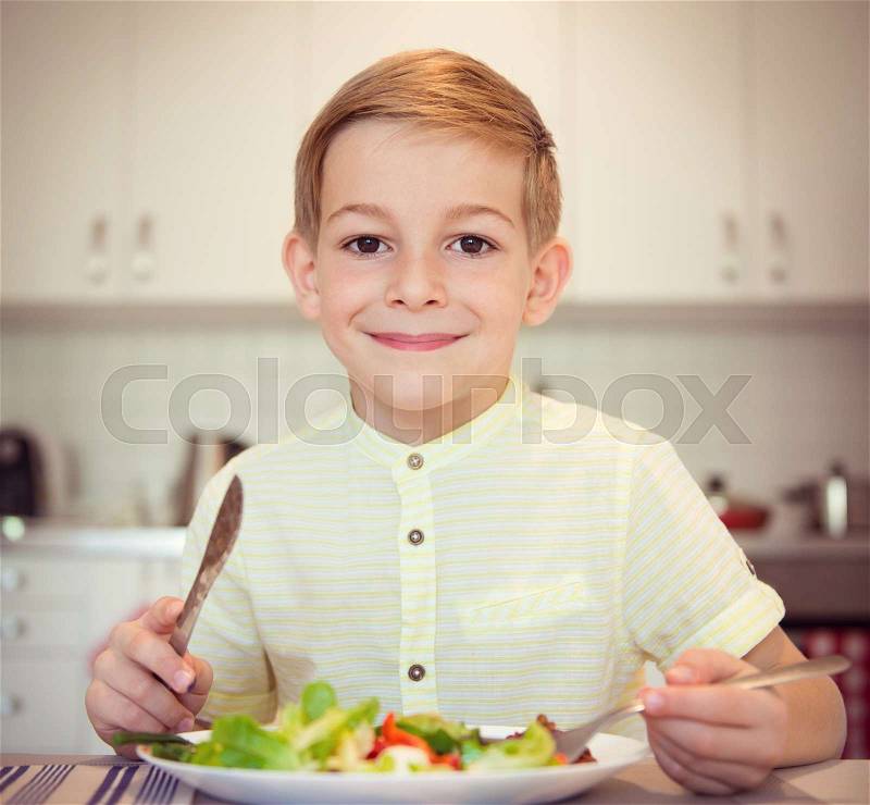 Young diligent boy at a table eating healthy meal using cutlery, stock photo