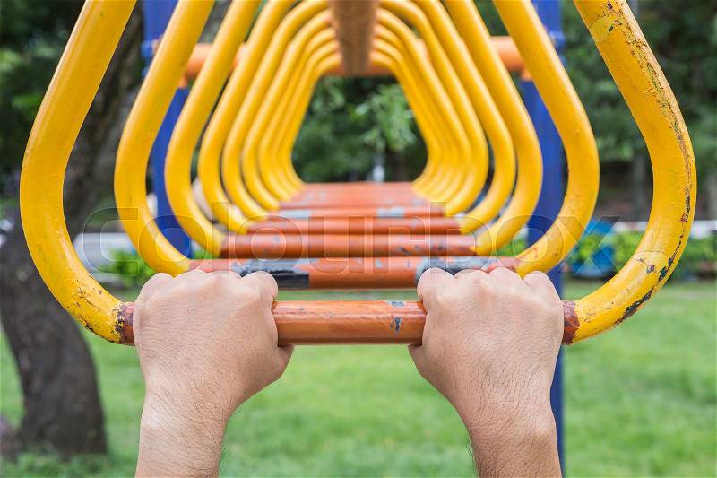 Close up hand hanging on steel bar for trapeze. Outdoor exercise equipment at public park, stock photo