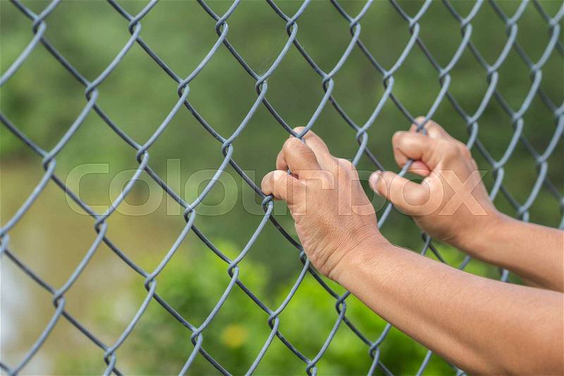 Close up hands hanging on metal chain link fence, stock photo
