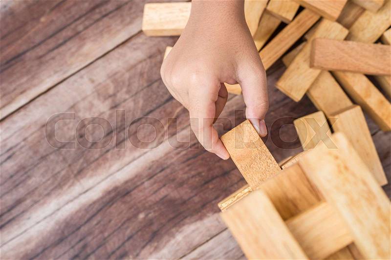 Close up hand holding blocks wood game (jenga) on wooden plank background. Risk concept, stock photo