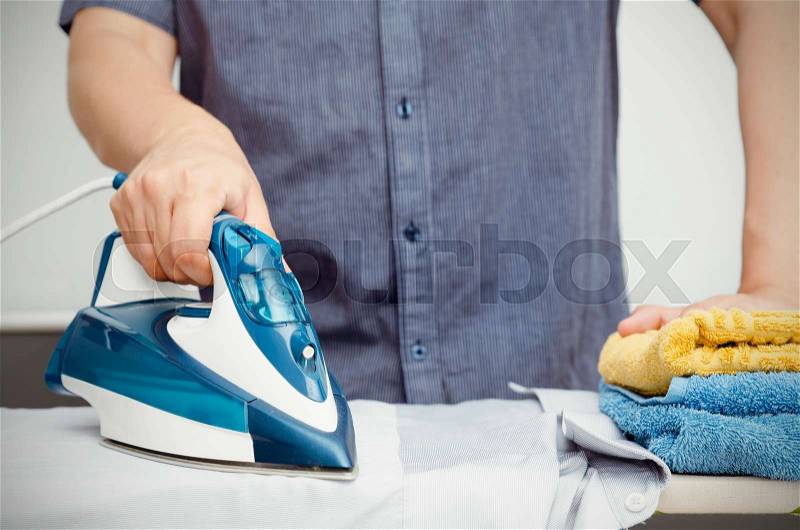 Man irons clothes on ironing board with steaming blue iron, stock photo