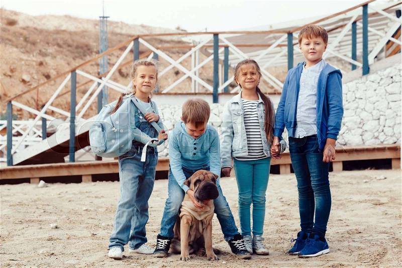 Group of fashion children wearing denim clothing with dog having fun on the sea shore. Autumn casual outfit in blue and navy color. 7-8 years old models, stock photo