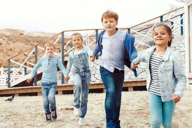Group of fashion children wearing denim clothing running on the sea shore. Autumn casual outfit in blue and navy color. 7-8 years old models, stock photo