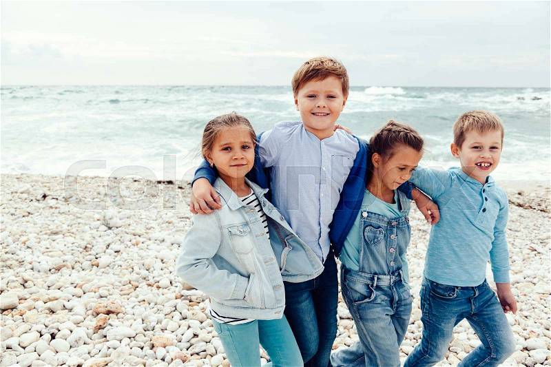 Group of fashion children wearing denim clothing having fun on the sea shore. Autumn casual outfit in blue and navy color. 7-8 years old models, stock photo