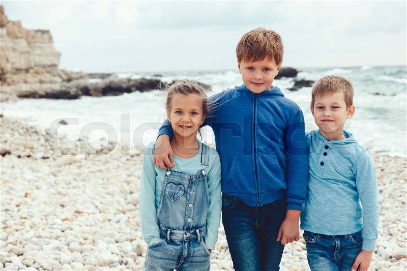 Group of fashion children wearing denim clothing having fun on the sea shore. Autumn casual outfit in blue and navy color. 7-8 years old models, stock photo
