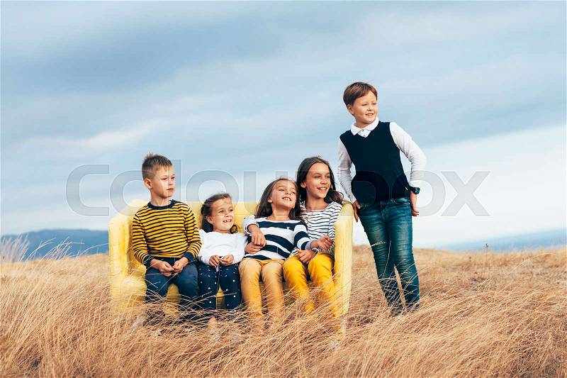 Group of fashion children wearing same style clothing resting on a sofa in the autumn field. Fall casual outfit in navy and yellow colors. 7-8, 8-9, 9-10 years old models sitting on a coach outdoor, stock photo