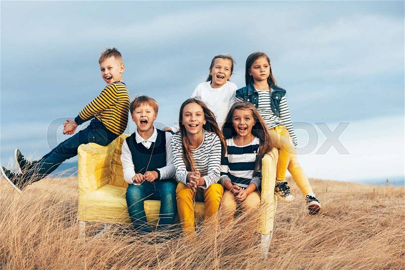 Group of fashion children wearing same style clothing resting on a sofa in the autumn field. Fall casual outfit in navy and yellow colors. 7-8, 8-9, 9-10 years old models sitting on a coach outdoor, stock photo