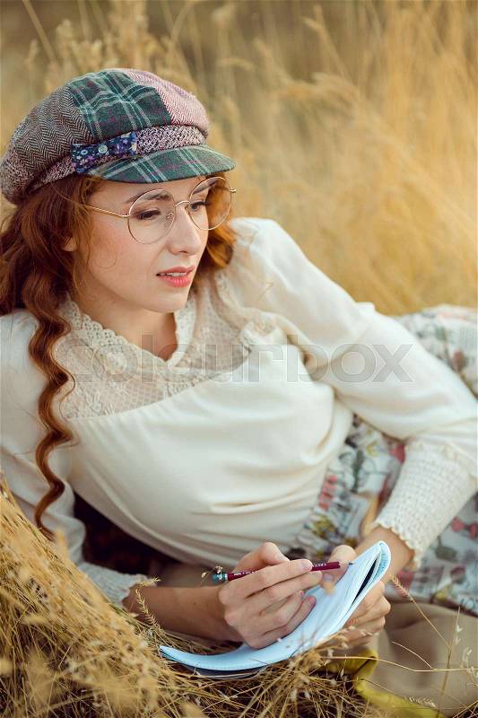 Woman writer concept. Student thinking and looking laying on yellow grass. Joyful happy girl sitting writing and reading outdoors on the nature, stock photo