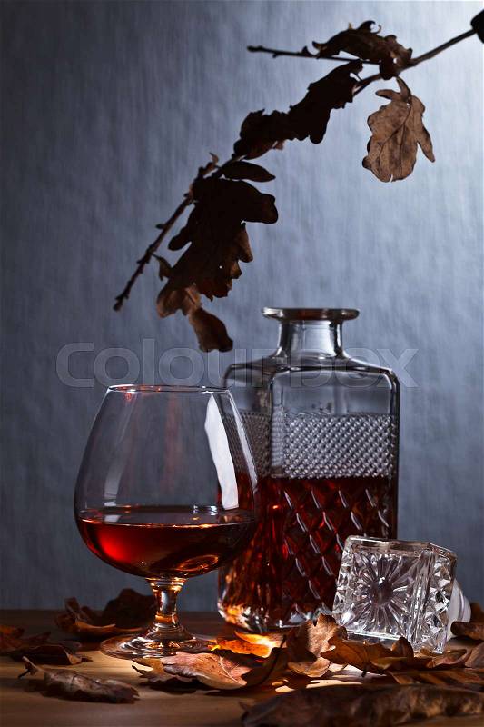 Snifter of brandy and dried oak leaves on wooden table, stock photo