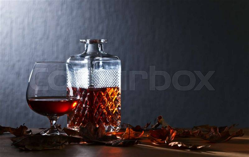 Snifter of brandy and dried oak leaves on wooden table, stock photo