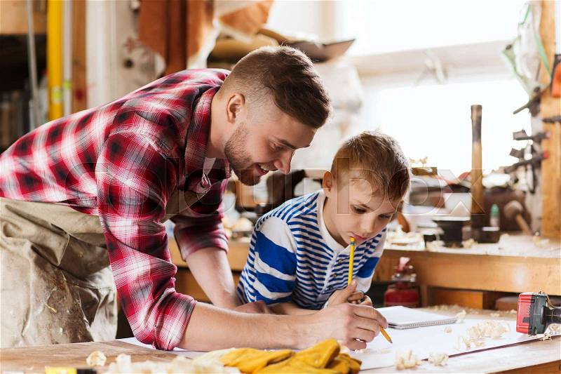 Family, carpentry, woodwork and people concept - happy father and little son with blueprint at workshop, stock photo