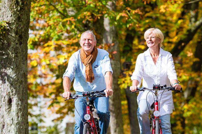 Senior couple, man and woman, on bicycles having bike tour in autumn park, stock photo