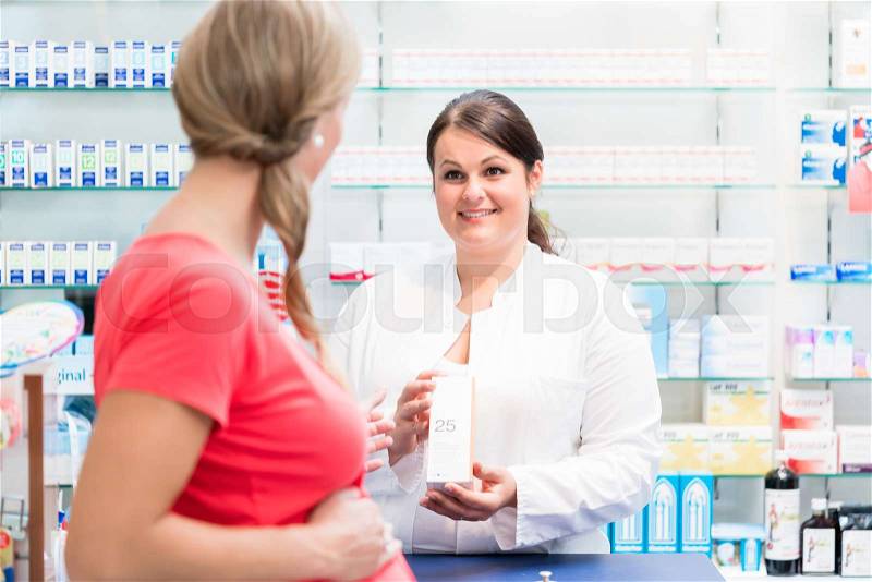 Pregnant woman buying medicine at chemist holding her baby belly, stock photo