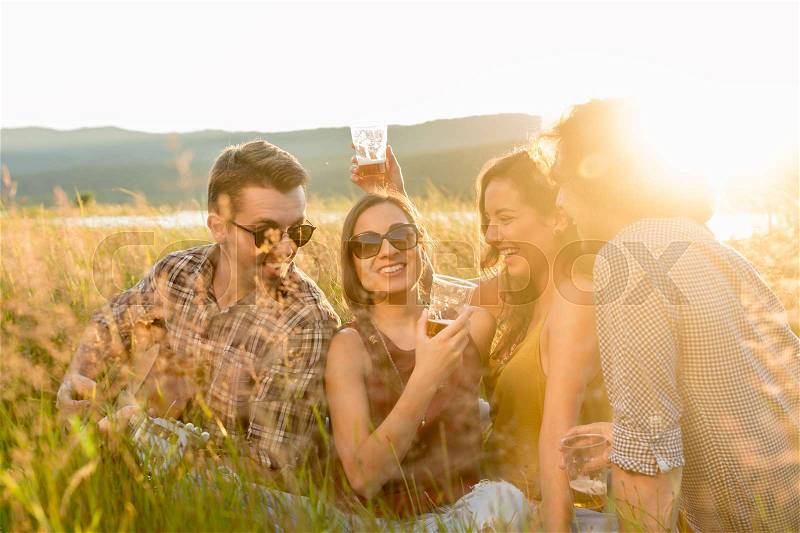 Friends enjoying evening mood of summer day sitting in high grass with drinks and guitar music, stock photo