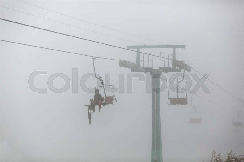 One passenger with bike and in equipping on chair lift in the fog, stock photo