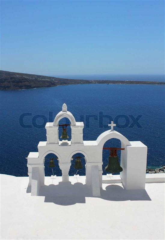 White bell tower of Greek church against blue sea and sky background, stock photo