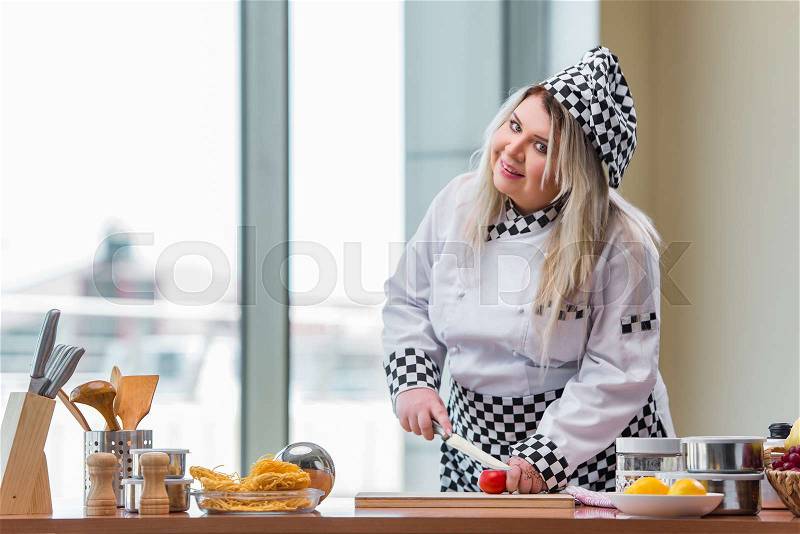Woman chef cutting tomato at the kitchen, stock photo