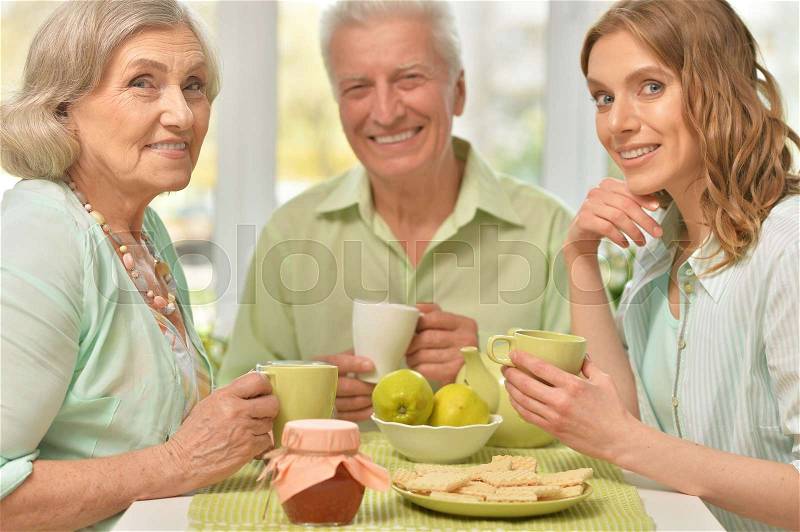 Cute family portrait of adult daughter with senior parents drinking tea, stock photo