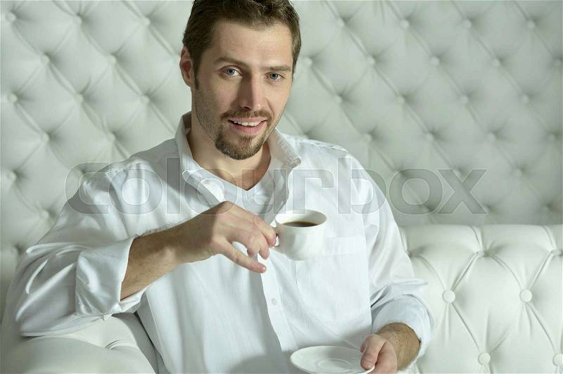Handsome casual man sitting on couch having coffee at home in the living room, stock photo