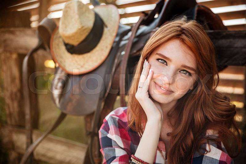 Close up portrait of a happy beautiful redhead cowgirl resting at the ranch fence, stock photo