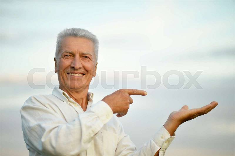 Happy senior man pointing on sky background, stock photo