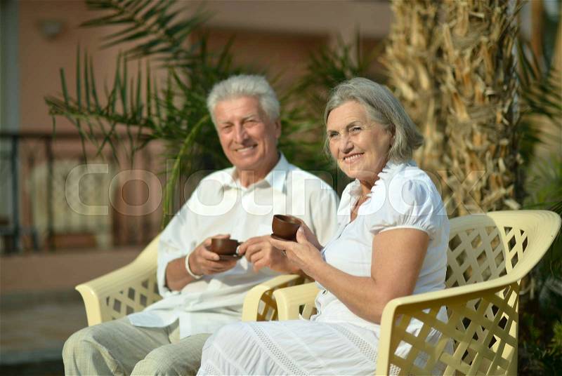 Loving senior couple sitting with coffee in tropical resort, stock photo