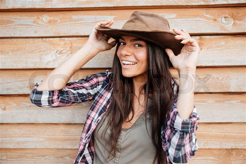 Closeup of happy beautiful young woman cowgirl in hat over wooden background, stock photo