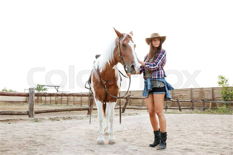 Cheerful cute young woman cowgirl walking with her horse in a farm, stock photo