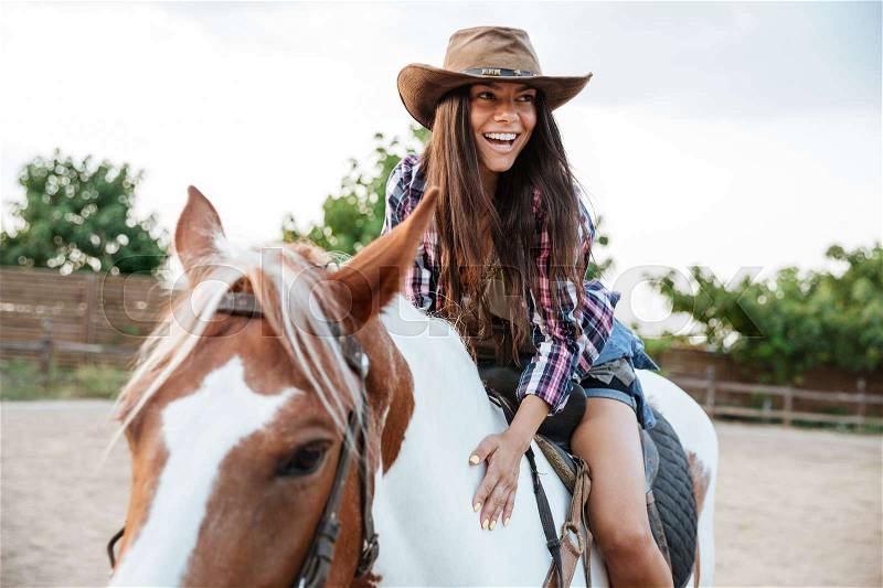 Smiling cute young womna cowgirl riding a horse outdoors and laughing, stock photo