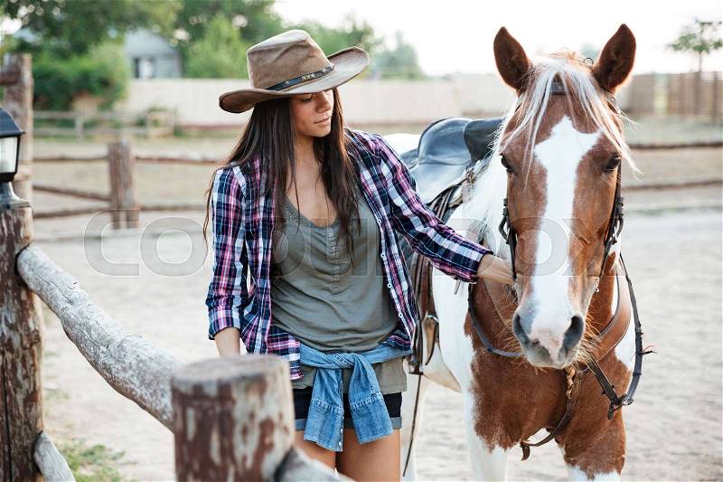 Beautiful young woman cowgirl walking with her horse on ranch, stock photo